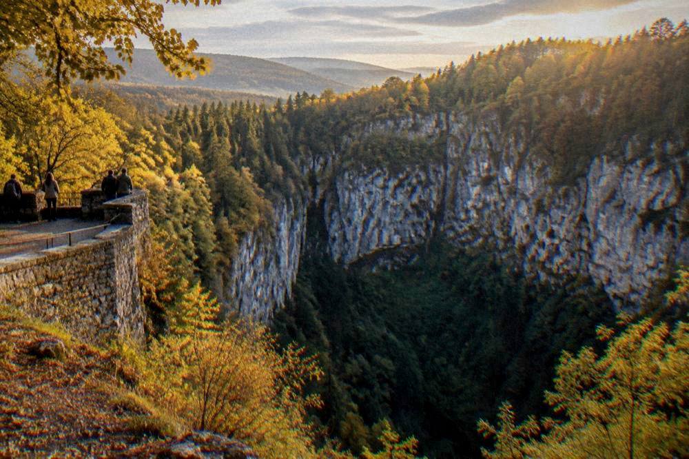 Sunlight falling over forested limestone hills under a partly cloudy sky
