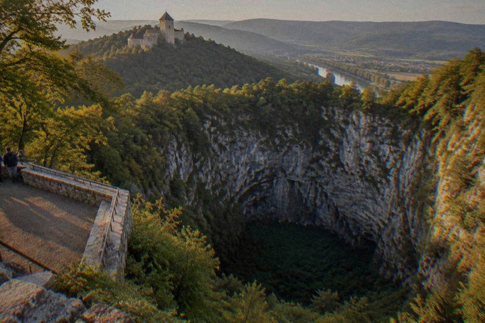 A stone castle on a forested hill above a river valley in South Moravia