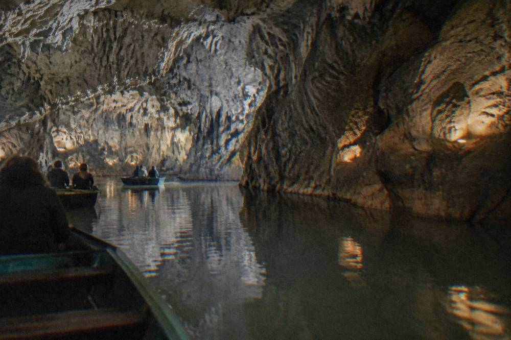 Boats floating on a quiet underground river inside a dimly lit limestone cave
