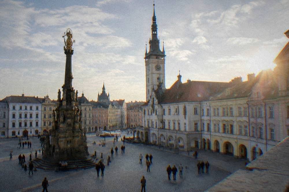 People walking across a cobblestone square between coloured baroque house facades in Olomouc