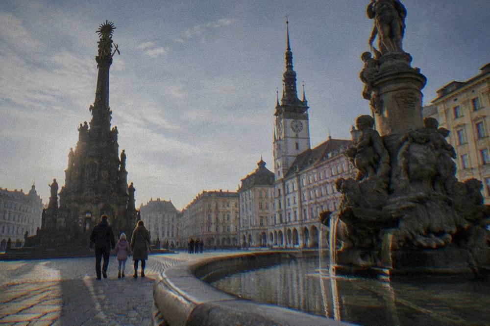 Family walking beside a baroque fountain in an Olomouc square