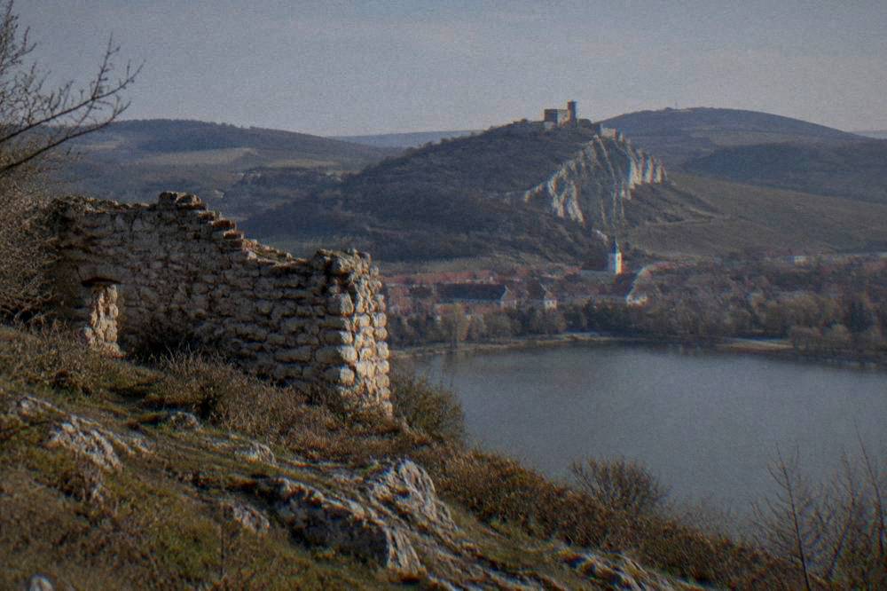 A hilltop castle above a small town with red roofs and vineyards on the surrounding hills