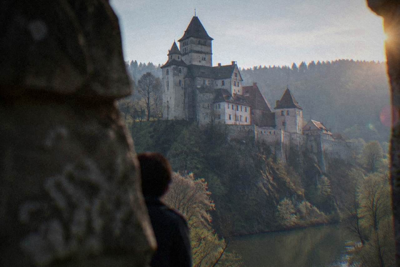 A stone castle with tall walls and towers rising above a forested hill