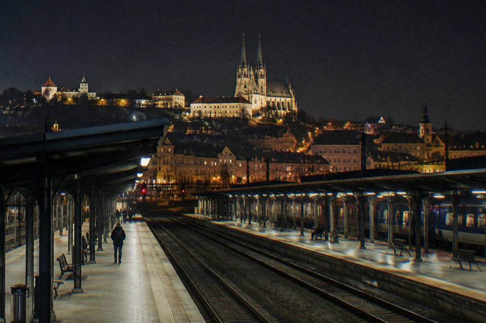 Two rail platforms at night with a city skyline glowing behind them