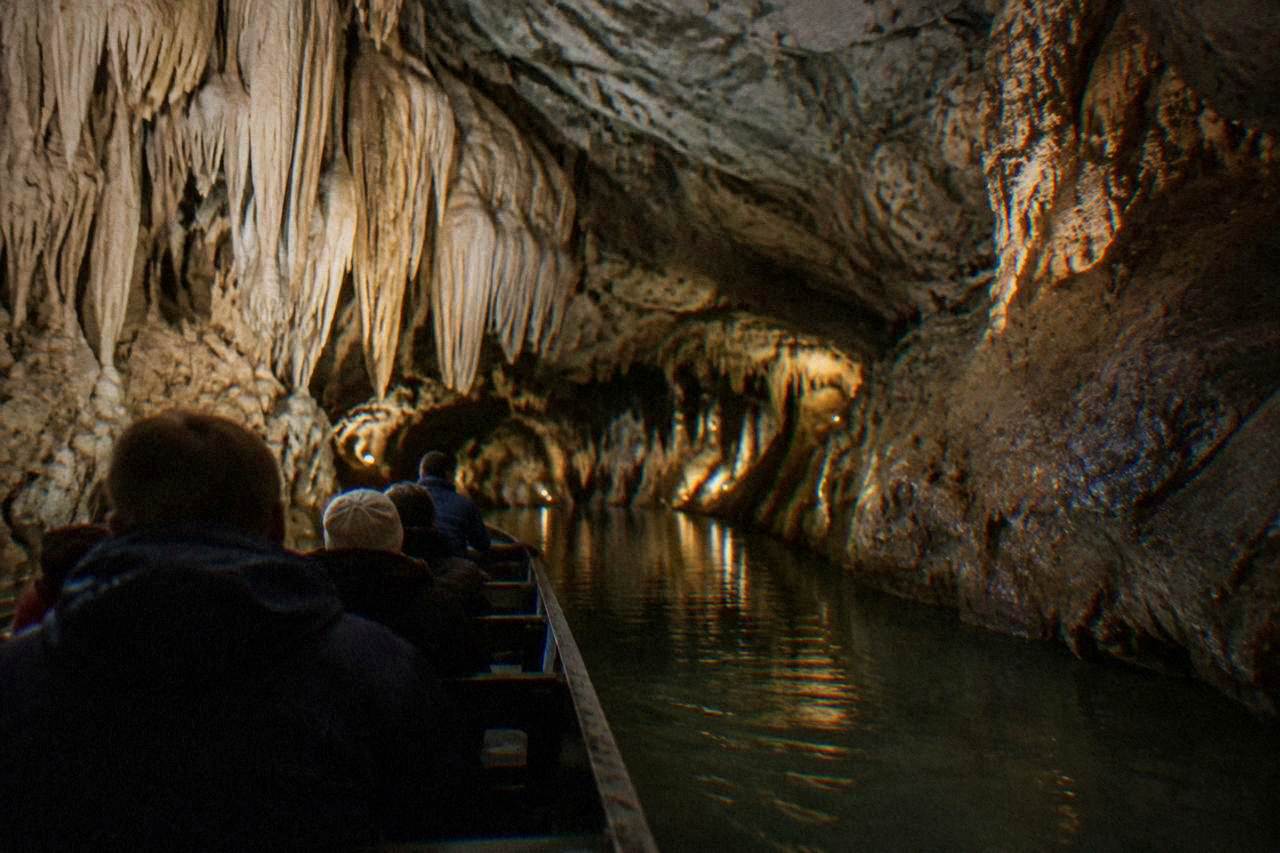 A boat carrying visitors along an underground river between rock walls inside a dimly lit limestone cave