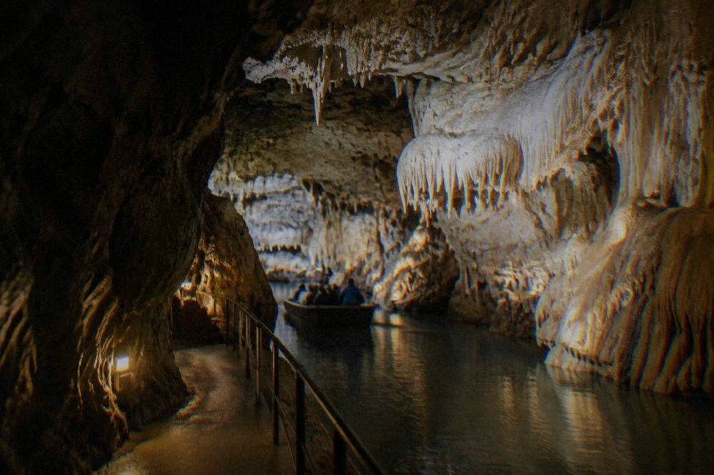 Illuminated limestone dripstone formations inside a cave passage with a walkway