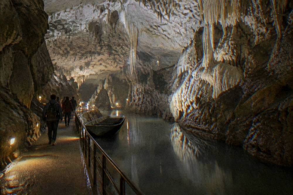 Visitors walking along a lit pathway through a limestone cave gallery