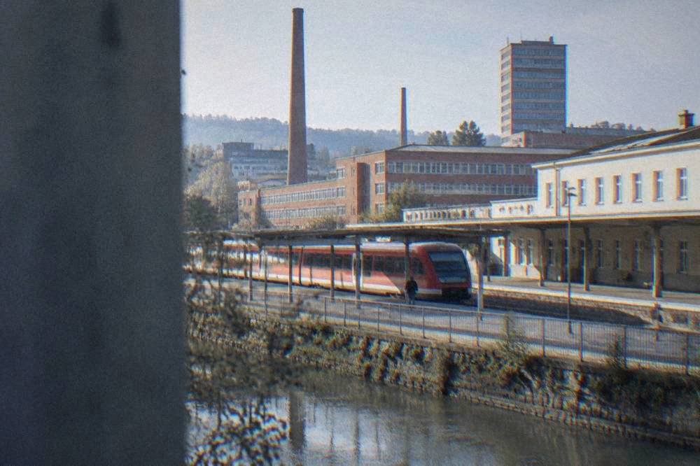 A red regional train waiting at a platform beside a Czech station building