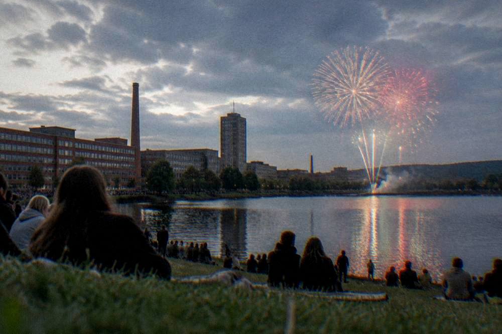 Fireworks bursting over a dark lake with crowds watching from the shore