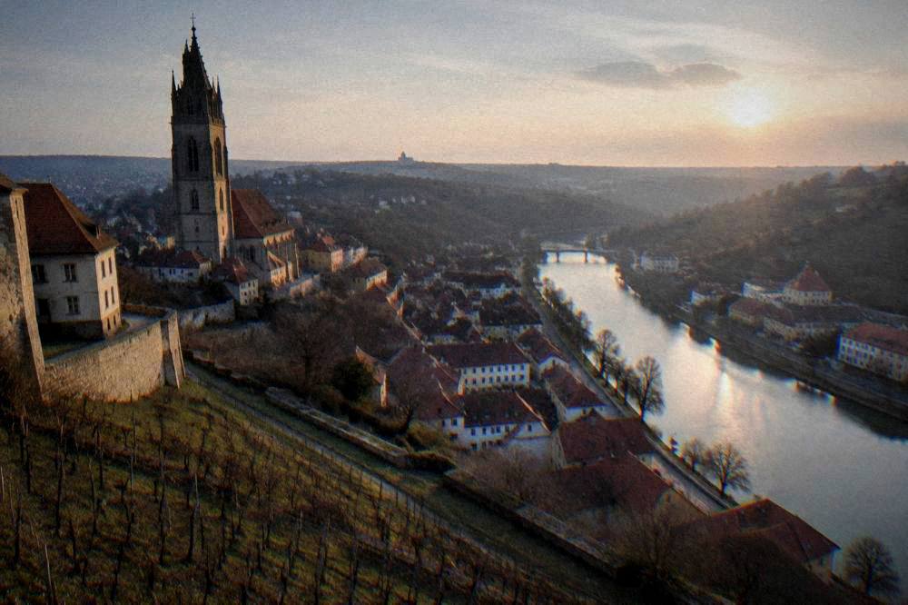 A viewpoint over a red-roofed old town and a winding river valley at sunset