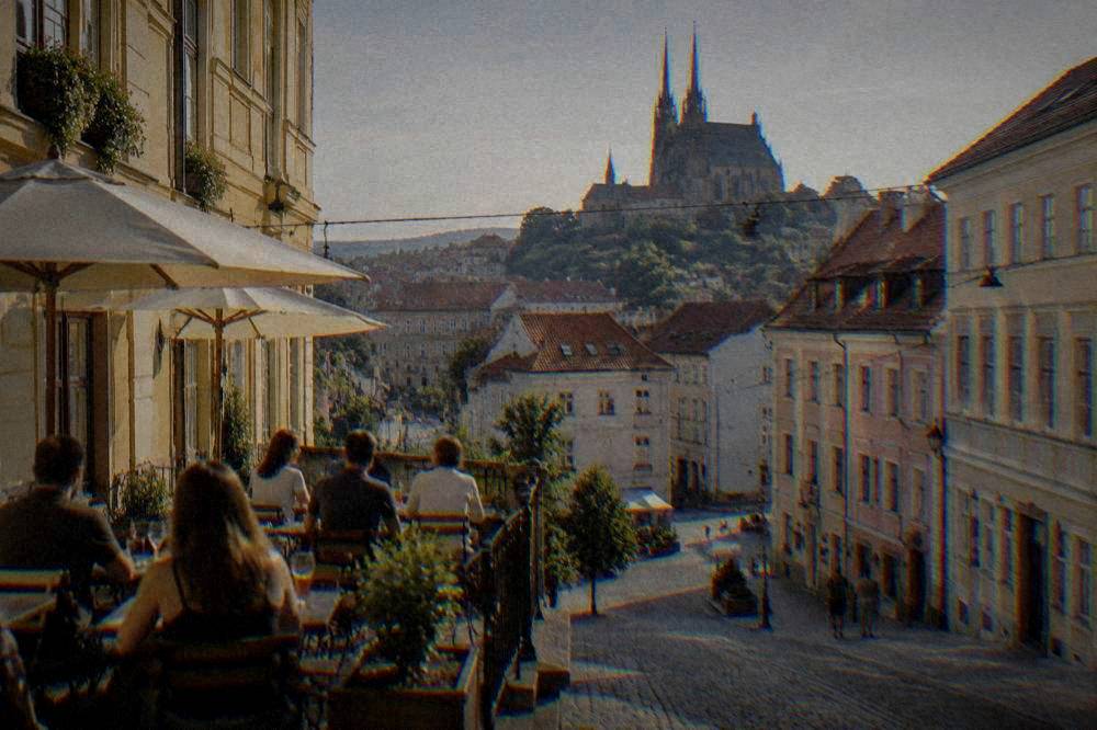 People at terrace tables in warm evening light on a Brno street