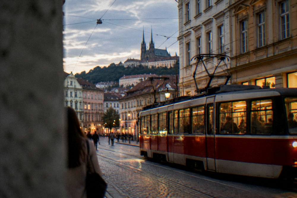 Tram passing lit shopfronts on a Brno street in the evening