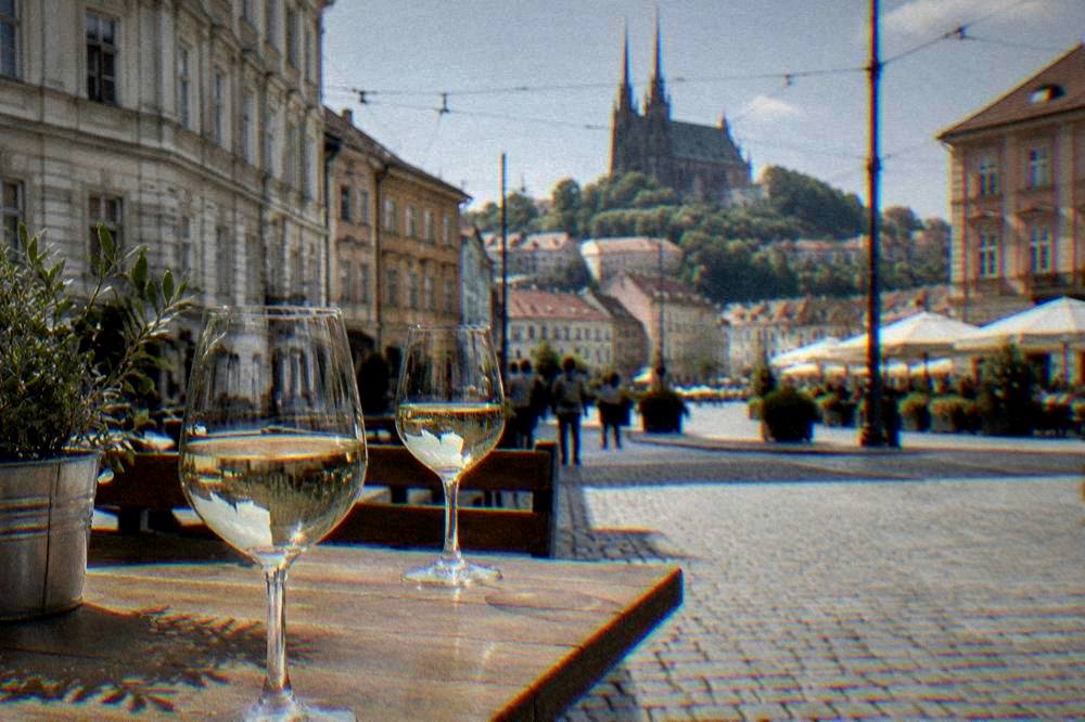 Glasses of white wine on a wooden table at an outdoor stall in a Brno square