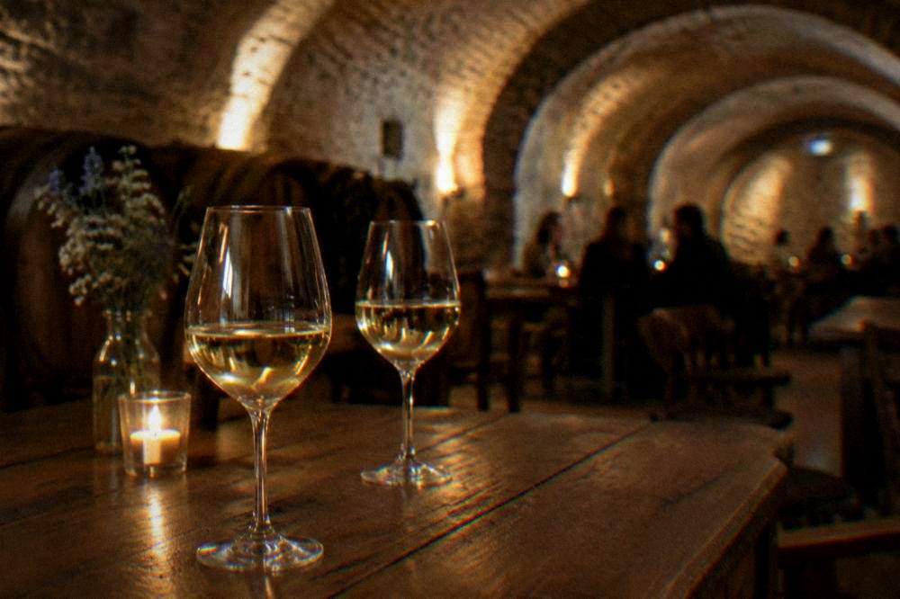Glasses of white wine on a wooden table in a vaulted cellar