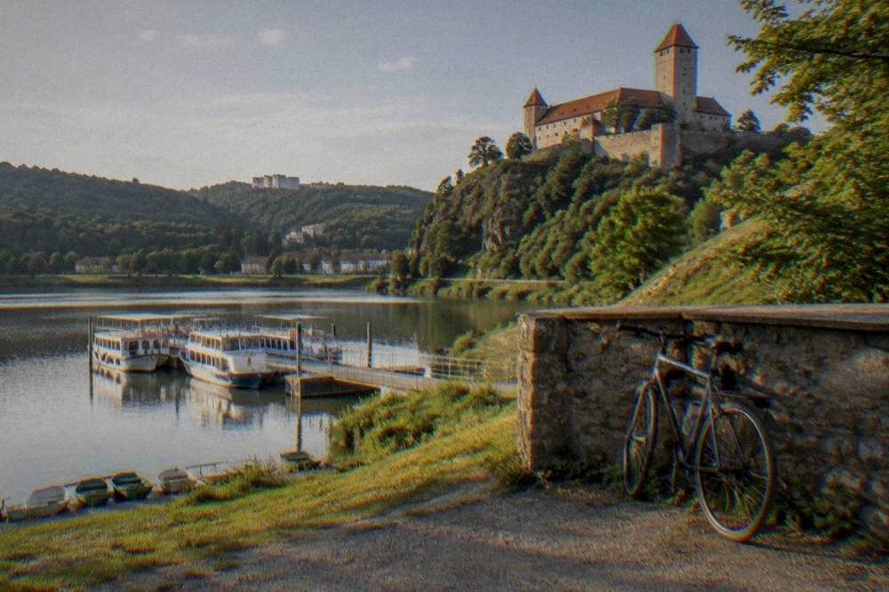 A bicycle leaning against a stone wall below a hilltop castle with tall walls and towers