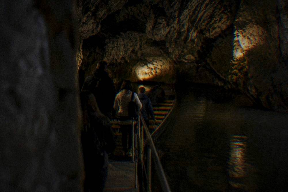 Cave visitors boarding a small boat on an underground river inside a dimly lit limestone cave