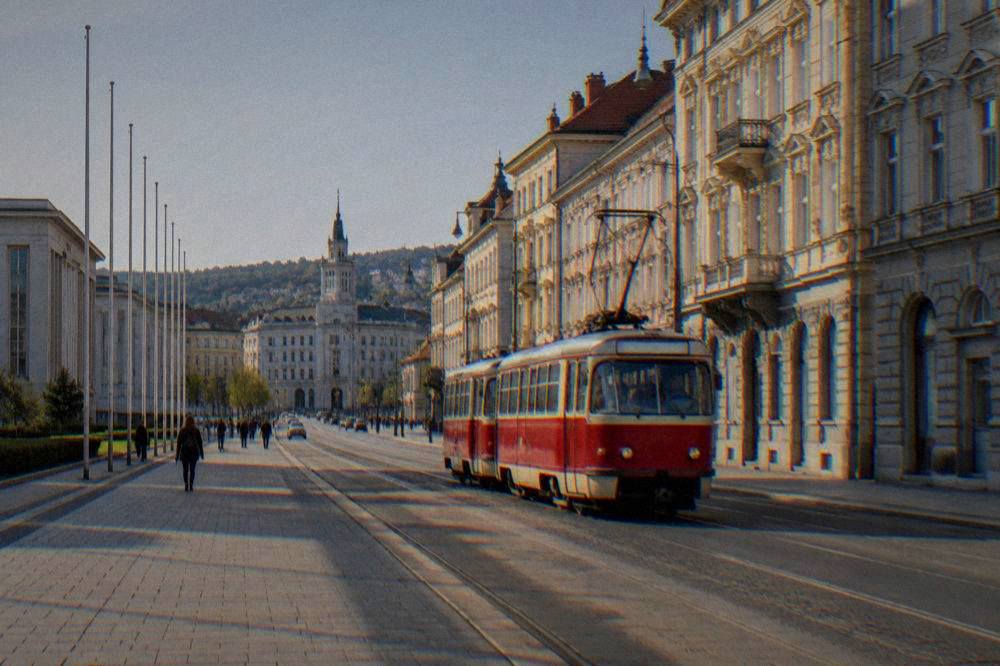 A red tram passing ornate facades on a busy street in late afternoon light