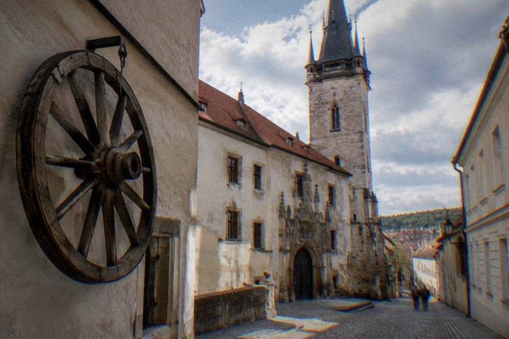 A large wooden cart wheel with wooden spokes hanging on a historic wall