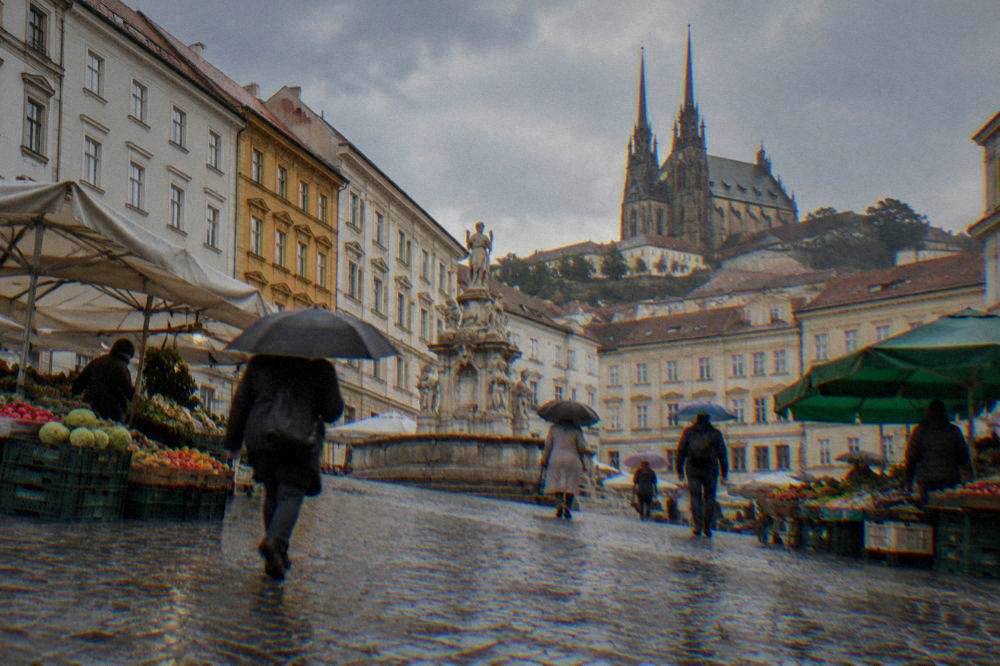 People with umbrellas crossing the Cabbage Market in Brno in light rain
