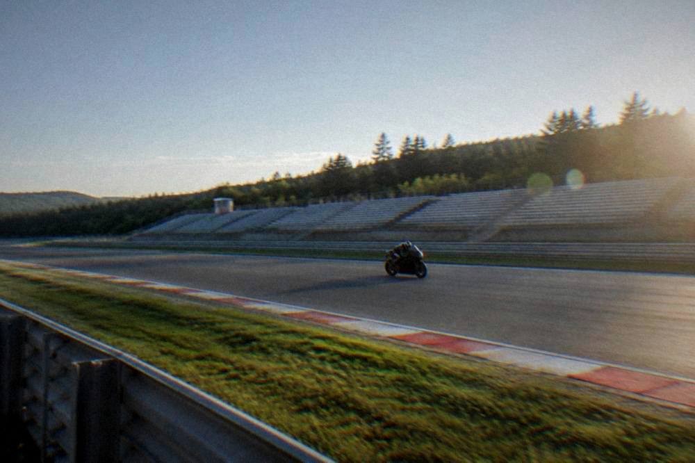 A motorcycle at speed on a circuit straight with blurred grandstands and clear sky