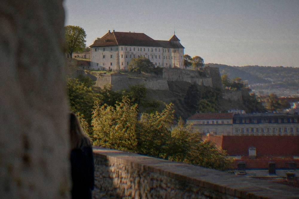 The stone walls and ramparts of Špilberk Castle above trees on a hill above Brno