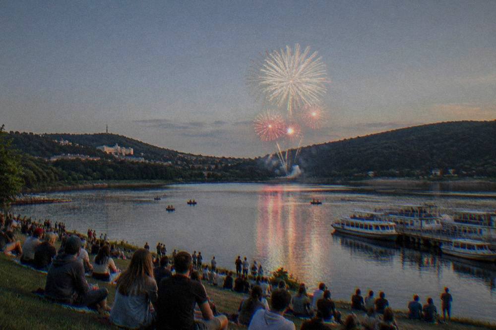 Fireworks bursting over the water of the Brno Reservoir at dusk with crowds watching from the shore