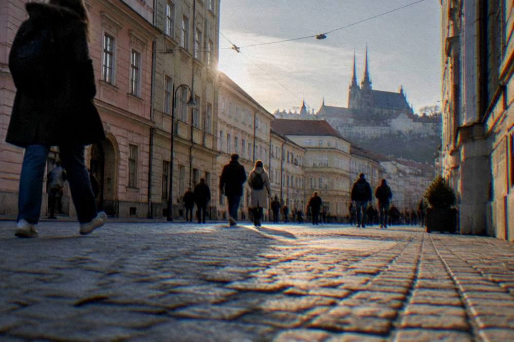 People strolling on a pedestrian street in central Brno past pastel facades at golden hour