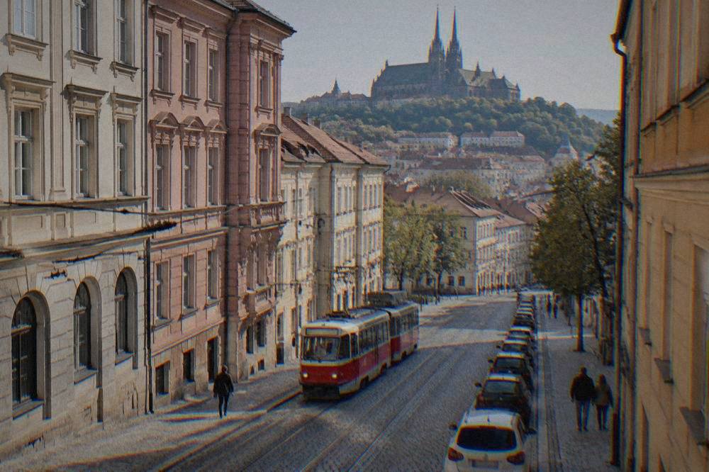A tram moving down a street in Brno past parked cars