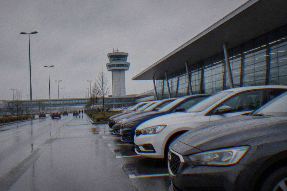 A row of rental cars parked in a lot beside an airport terminal