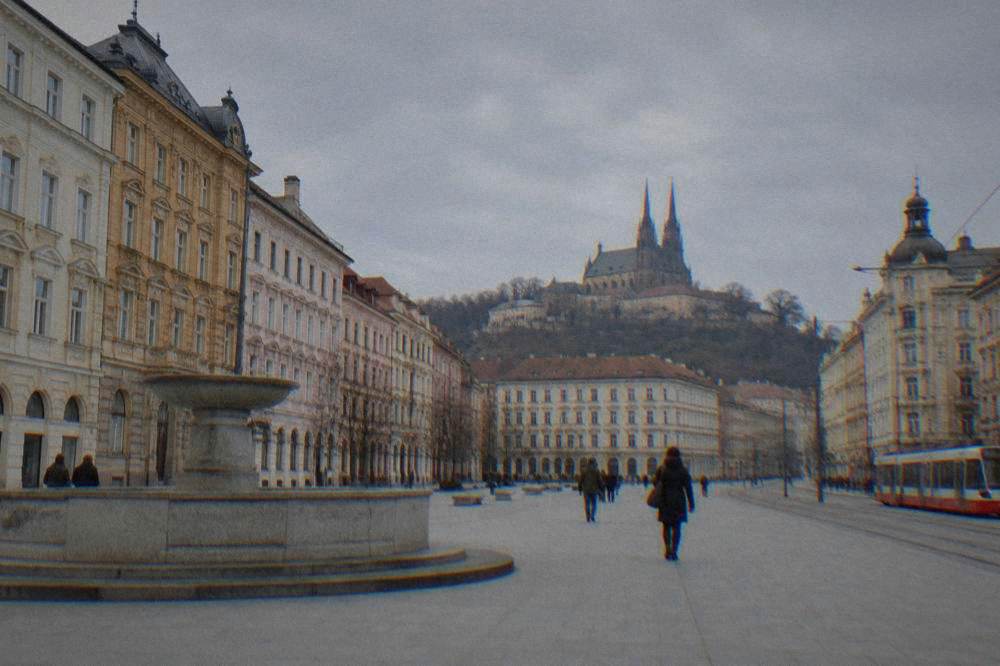 A stone castle on a hill above a city skyline with twin spires in the distance