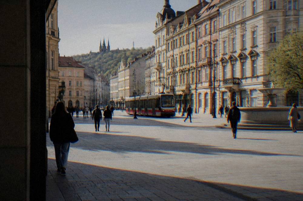 A tram moving down a city street lined with pastel coloured facades and pedestrians