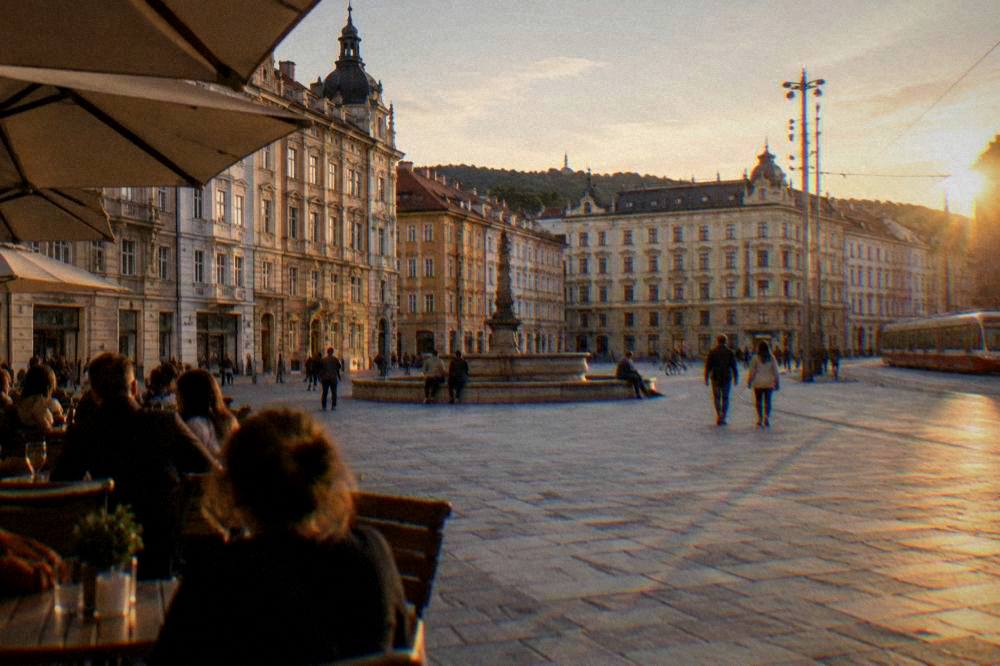 An evening city square with illuminated facades and people sitting at outdoor tables