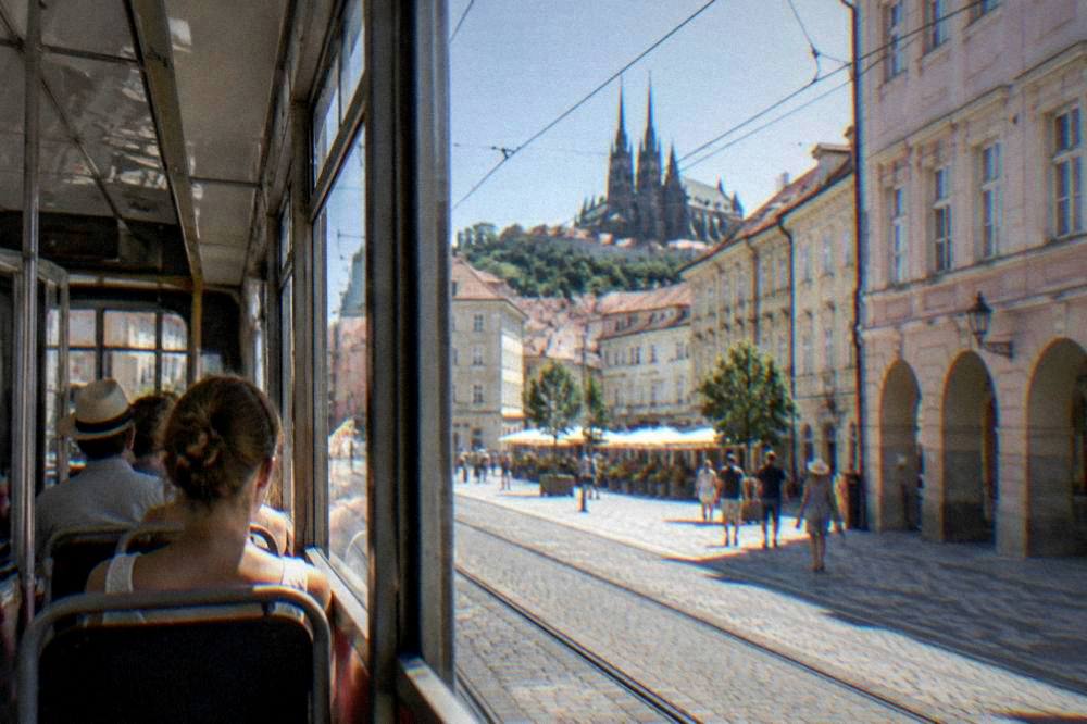 Travellers on a Brno tram in summer passing colourful old town buildings