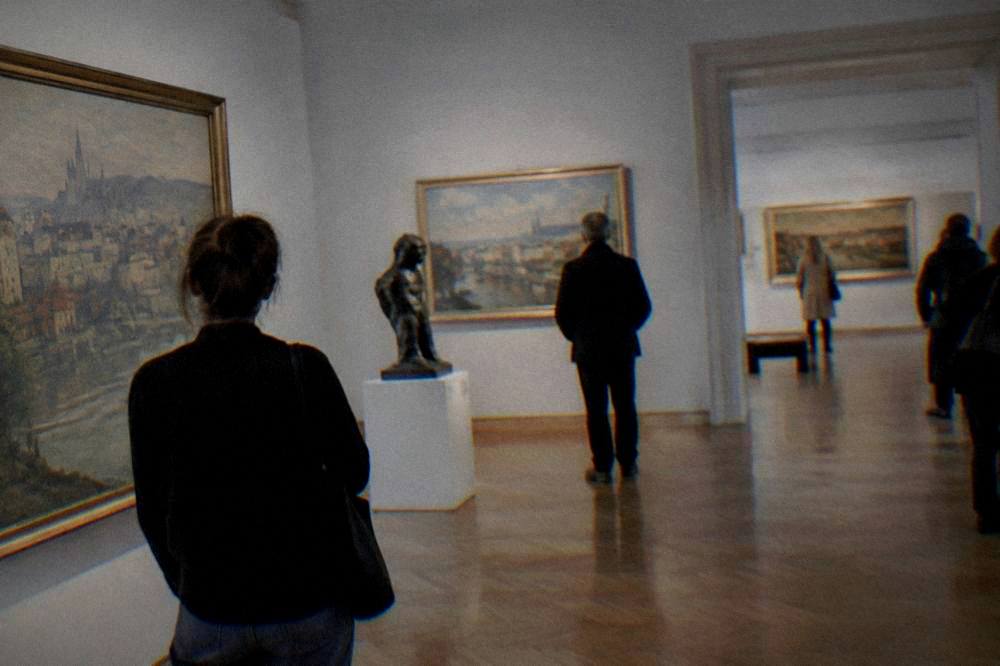 Interior of a Brno museum gallery with visitors looking at exhibits on a rainy day