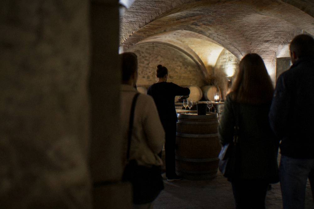 A guide pouring wine for a small group standing around a barrel in a vaulted cellar