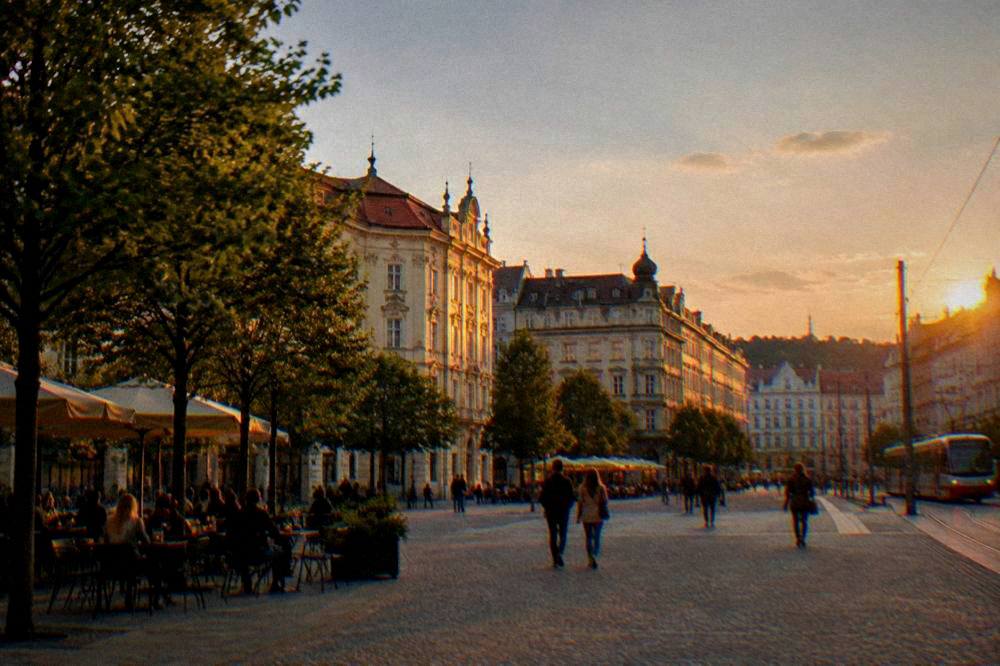 A historic square at dusk with people walking past illuminated facades and outdoor tables