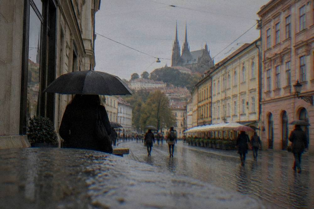 A rainy street in Brno with umbrellas outside shops