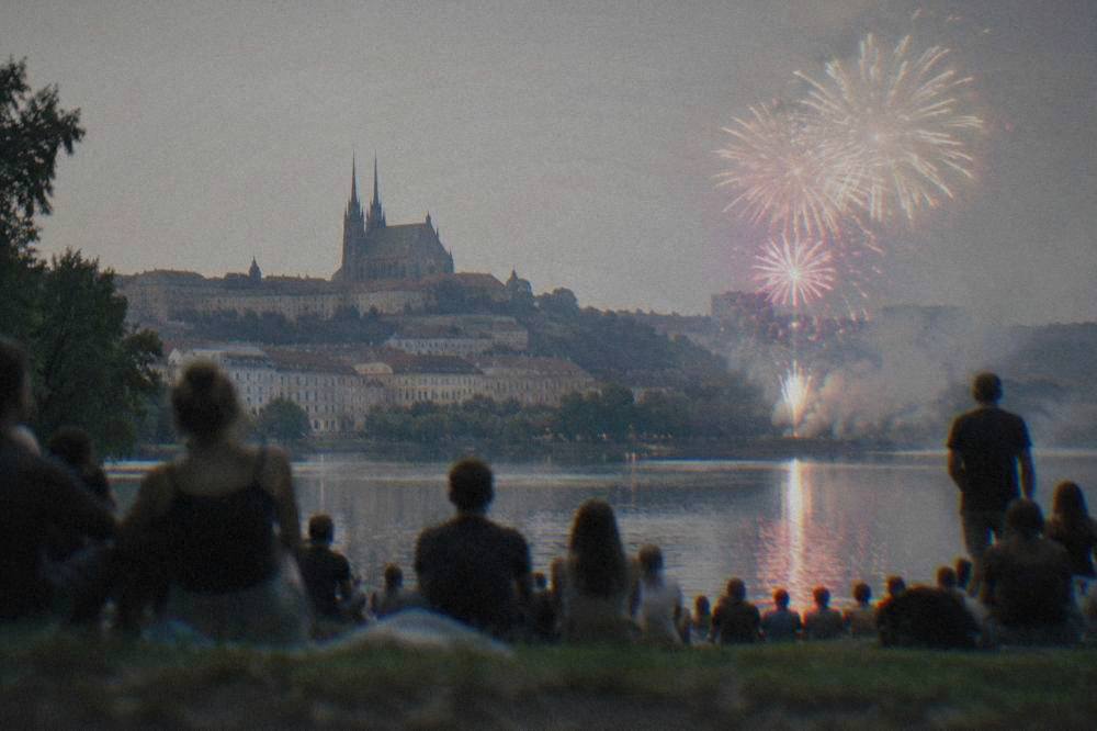 Fireworks bursting over a dark lake with silhouetted crowd on the shore