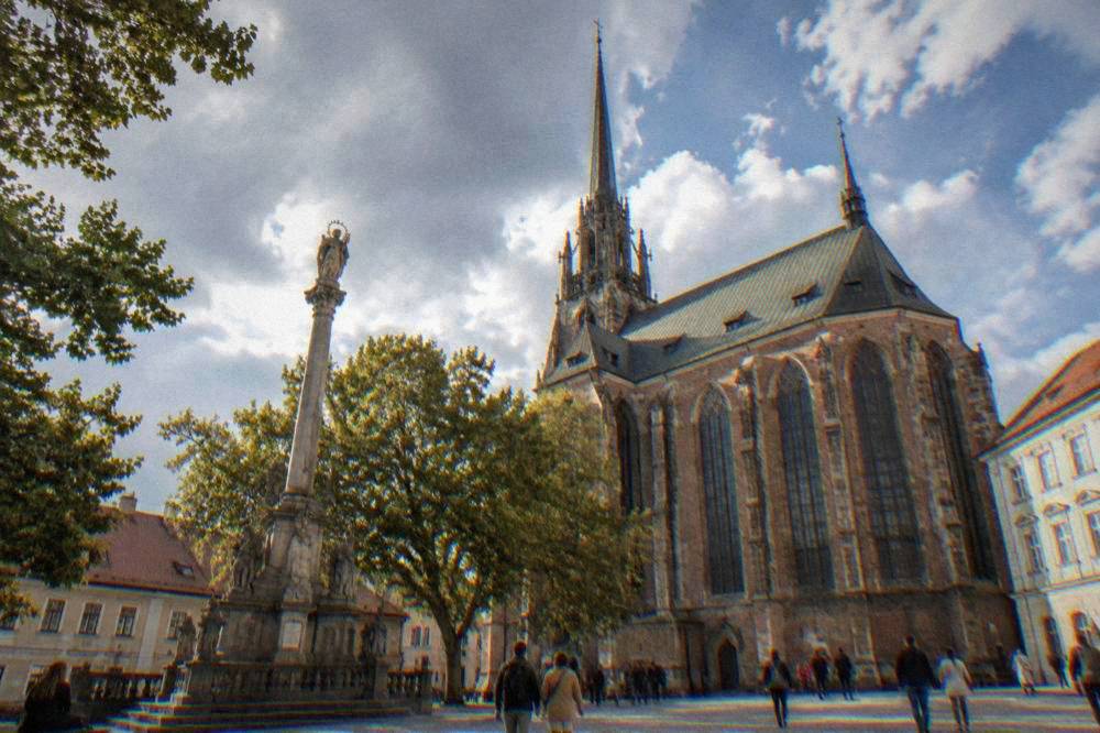 Visitors walking beside the brick Gothic front of the Basilica of the Assumption in Old Brno