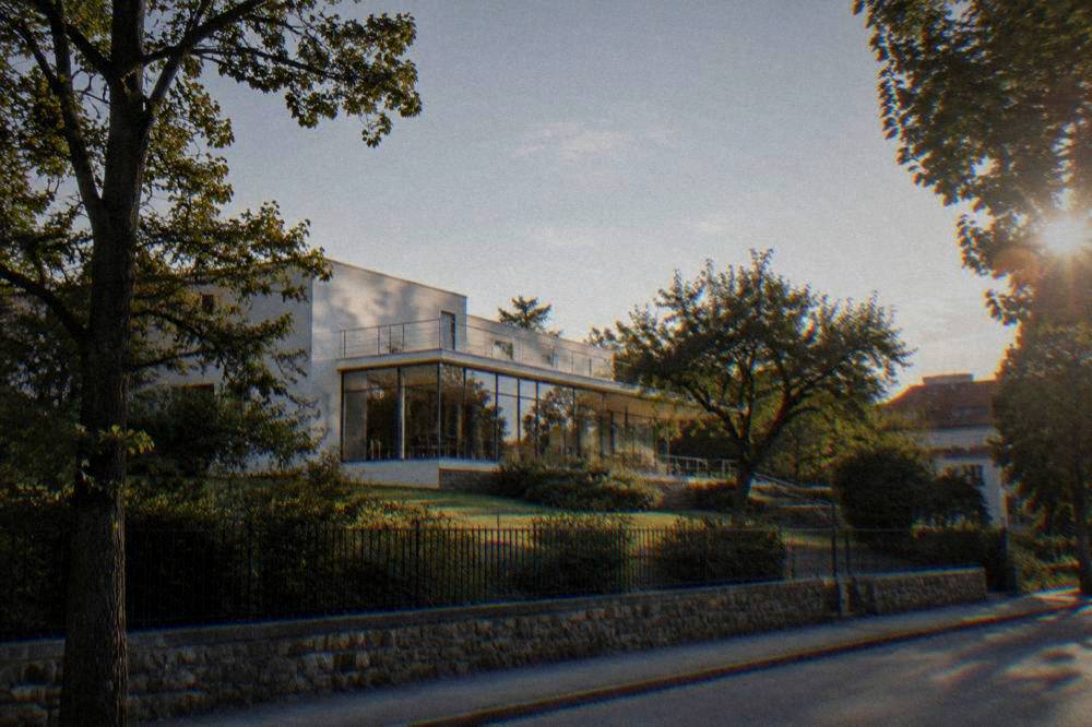 The modernist glass facade of Villa Tugendhat set among trees in a residential street