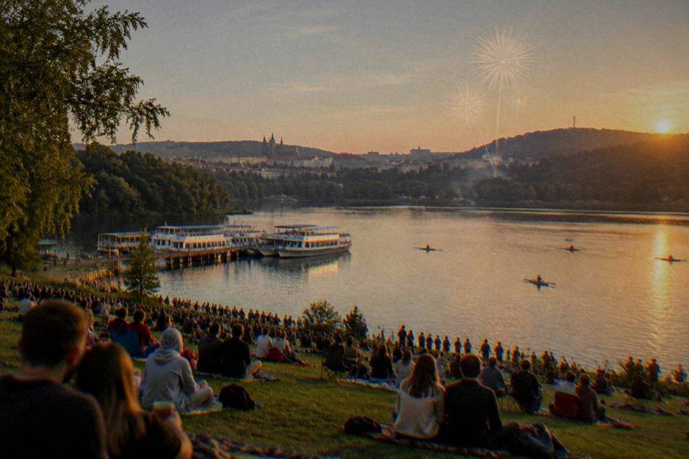 Crowds gathered on a grassy lakeshore waiting for an evening fireworks show
