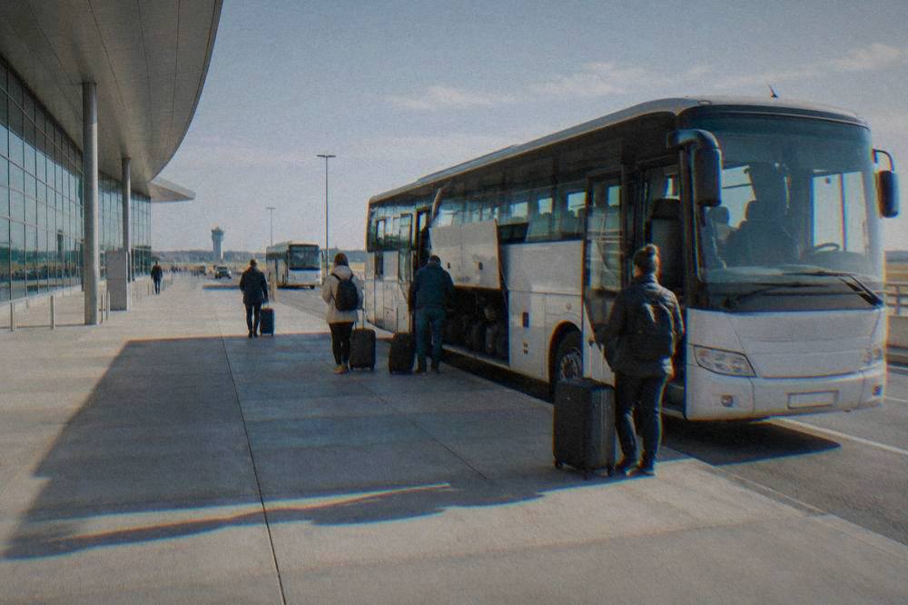 A regional bus parked at an airport terminal forecourt with passengers loading luggage