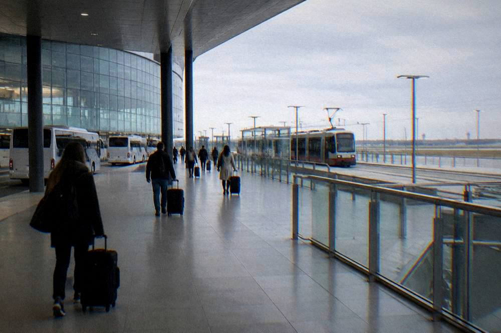 Travellers with suitcases walking through a station concourse towards tram platforms