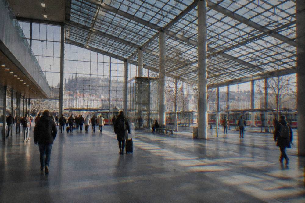 The glass roof of a large railway hall with travellers walking below