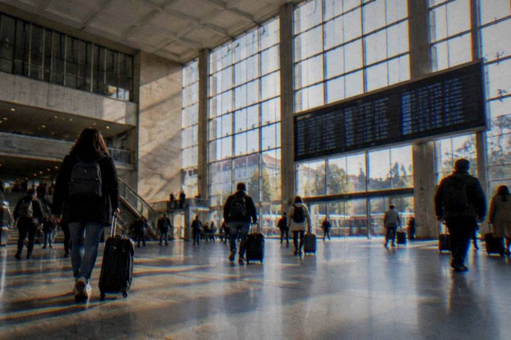 A station concourse with departures board and travellers with luggage