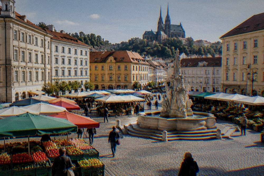 Market stalls with fruit and vegetables under coloured awnings on a cobbled square