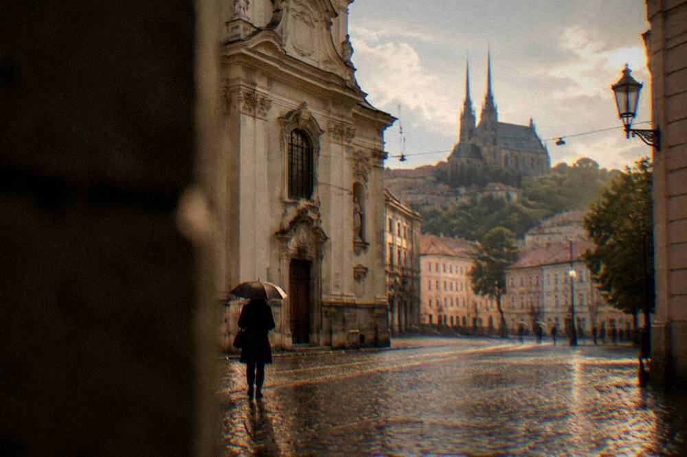 Person with an umbrella walking past a baroque church facade in Brno in light rain