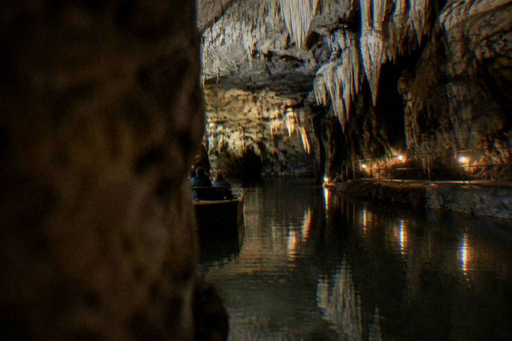 Underground cave lake inside the Punkva Caves with a small boat and dim walkway lighting
