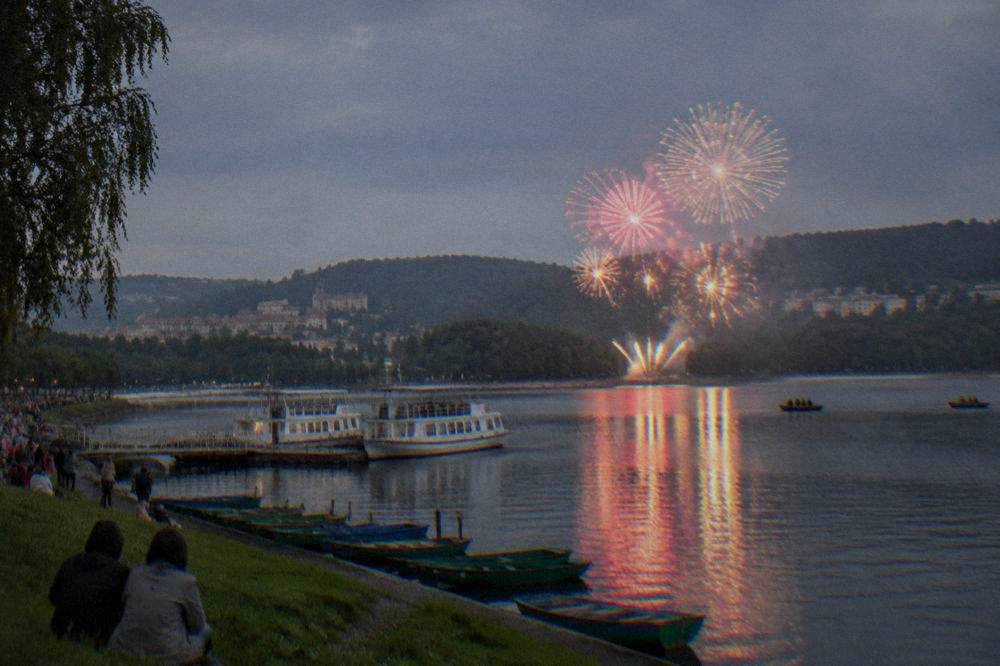 Fireworks bursting over the water of the Brno Reservoir at night with crowds along the shore