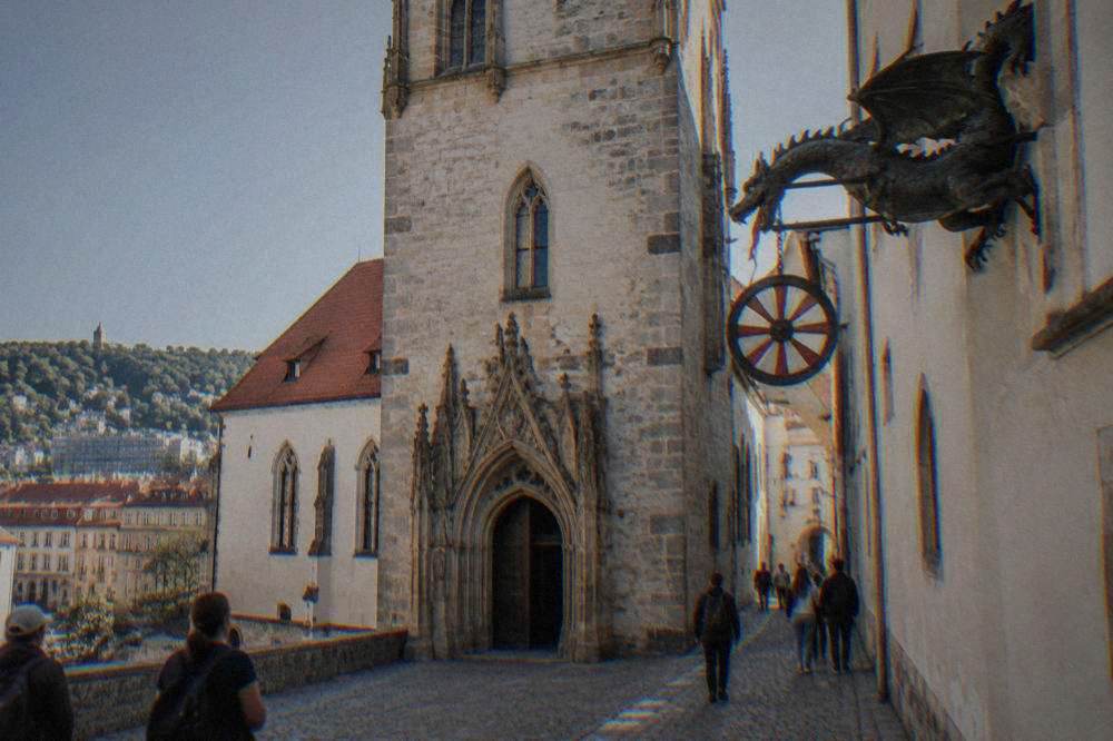The Brno dragon and painted wheel hanging in the Old Town Hall passage with visitors below